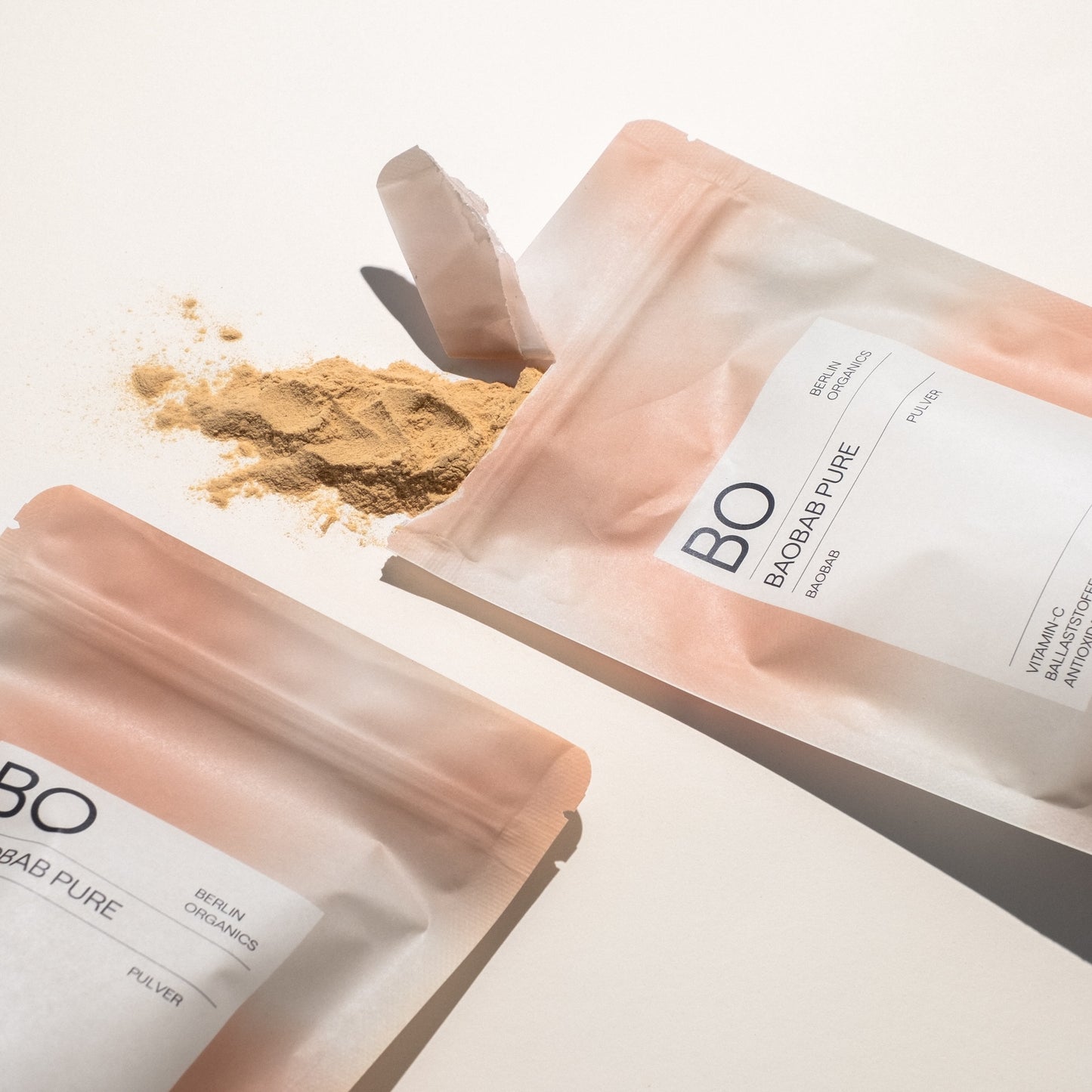 Offene Verpackung von Baobab Pure mit verstreutem hellbeigem Pulver auf weißem Untergrund.